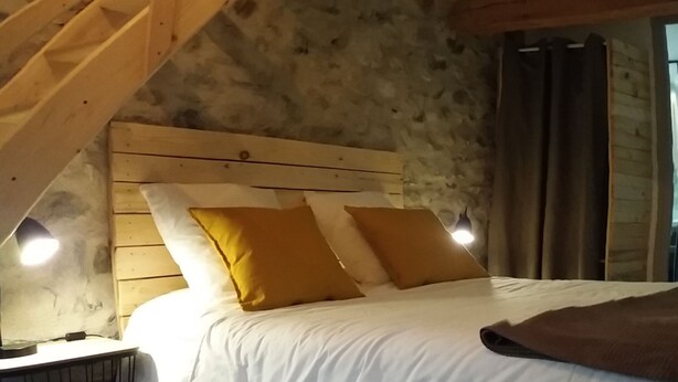 Een slaapkamer met een houten trap, een bed met witte beddengoed en gele kussens, en een nachtkastje met een lamp.