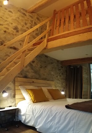 Ein Schlafzimmer mit einer Holztreppe, einem Bett mit weißer Bettwäsche und gelben Kissen sowie einem Nachttisch mit einer Lampe.
