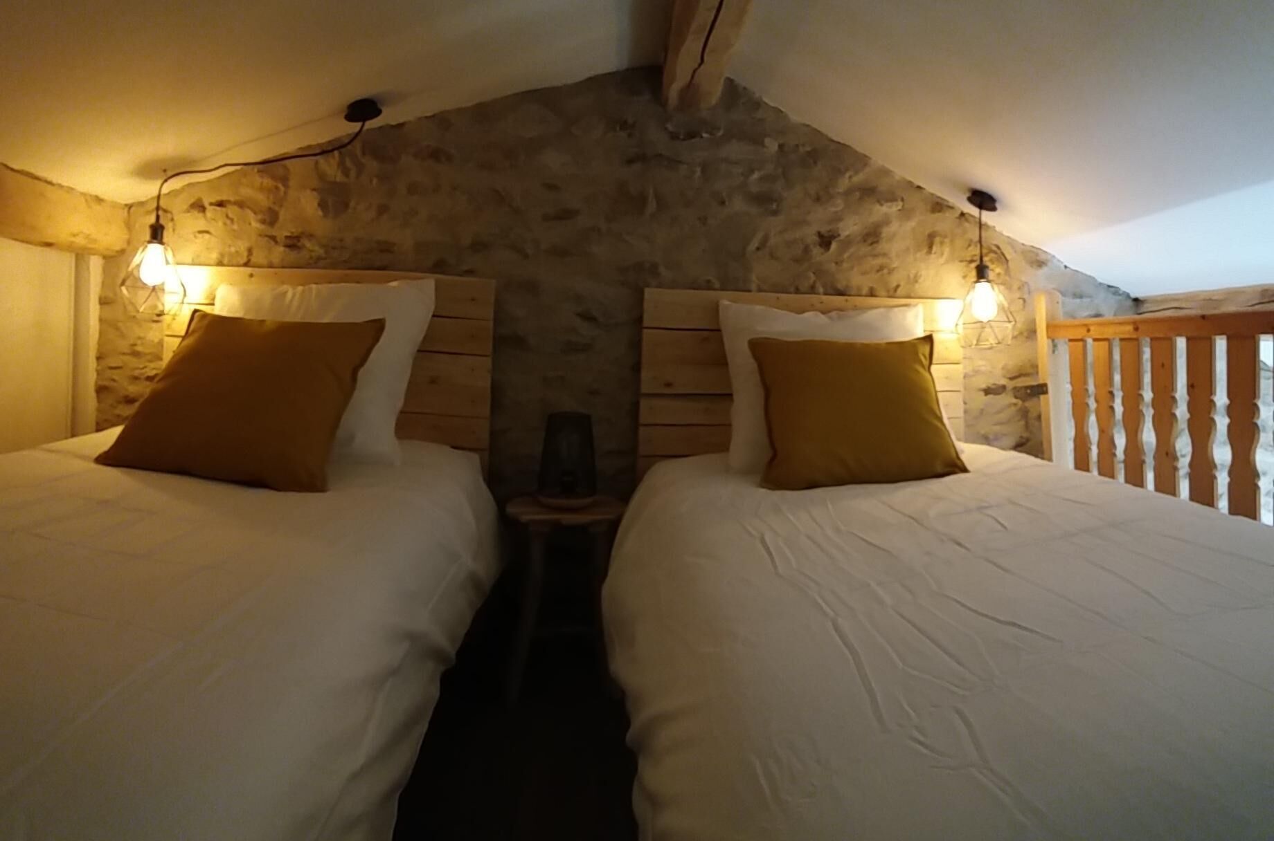 Une chambre confortable avec deux lits, des murs en pierre, des têtes de lit en bois et un balcon doté d’une balustrade en bois.