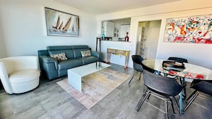 Una sala moderna con un sofá gris, una mesa de centro blanca y una zona de comedor con una mesa de vidrio y sillas negras.