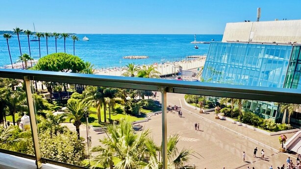 Vista costera con playa, palmeras y un edificio moderno de cristal.