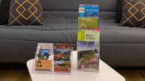 Een moderne woonkamer met een grijze bank, twee decoratieve kussens en een salontafel met brochures en ansichtkaarten.