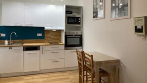 Een moderne keuken met witte kasten, een magnetron, oven en een eethoek met een tafel en stoelen.