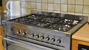 Ein Edelstahl-Kochfeld mit mehreren Flammen und Reglern, eine Kaffeemaschine und eine geflieste Spritzschutzwand.