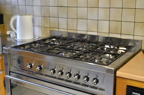 Une cuisinière de cuisine en acier inoxydable dotée de plusieurs brûleurs et de plusieurs boutons, une machine à café et un pare-feu carrelé.