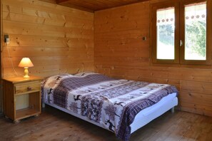 Une chambre dans un chalet en bois, avec un lit, une table de chevet avec une lampe et une fenêtre donnant sur la forêt.