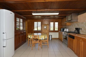 Een keuken met houten kastjes, een witte koelkast, een eettafel met stoelen en een betegelde vloer.