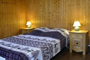 A wooden-paneled room with a bed, two bedside tables with lamps, and a nightstand with a drawer.