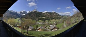 Une vue panoramique d’un village de montagne aux maisons traditionnelles, avec un ciel dégagé et des sommets enneigés à l’horizon.