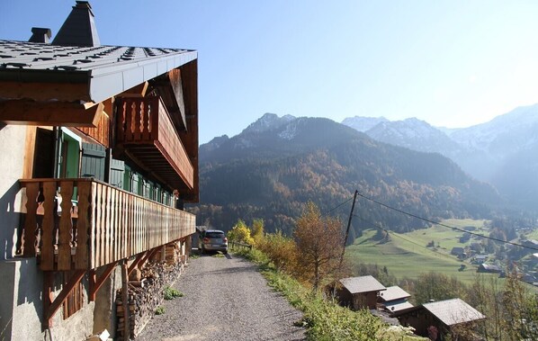 A mountain road with a wooden building on the left and a view of mountains in the background.