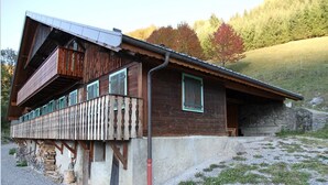Une cabane en bois dotée d’un balcon, de fondations en pierre et d’une entrée surmontée d’un mur en pierre.