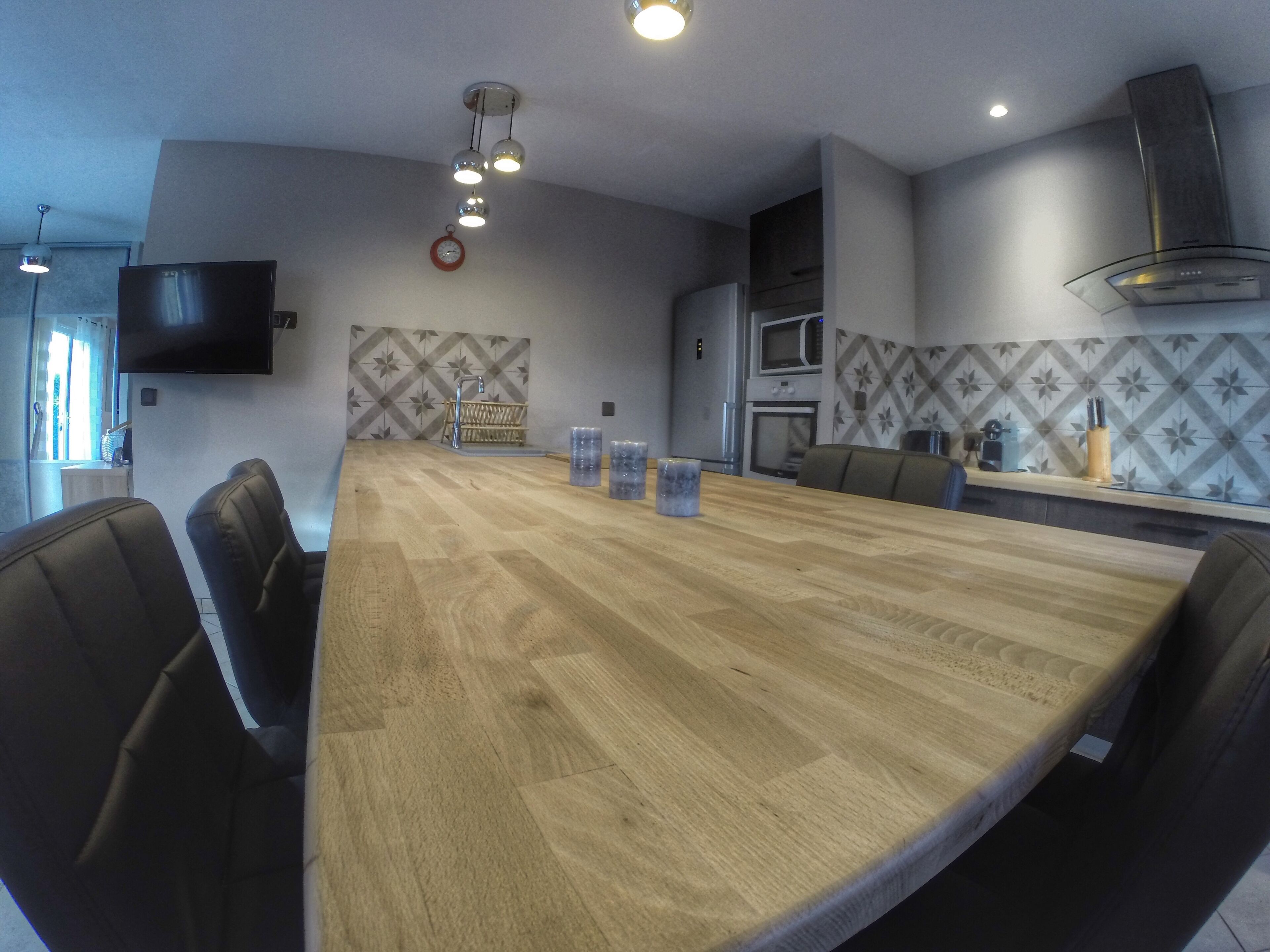 A modern kitchen with a large wooden table, built-in appliances, and a TV mounted on the wall.