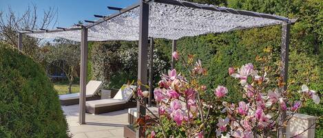 Eine Garten-Terrasse mit Pergola, Sitzbereich und blühenden Pflanzen.