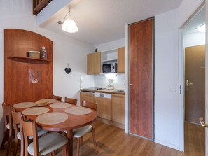 Uma cozinha compacta com armários de madeira, micro-ondas e fogão. Há uma mesa de jantar com cadeiras e um lustre.