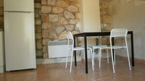 A small kitchen with a white refrigerator, a stone wall, a tiled floor, and a table with two white chairs. - Domaine de La Tourelle, grand studio (Lorgues)