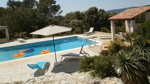 A swimming pool with lounge chairs and an umbrella, surrounded by greenery and a tiled roof structure. - Domaine de La Tourelle, grand studio (Lorgues)