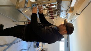 Eine Person bedient eine Maschine in einer Werkstatt, mit sichtbaren Metallkonstruktionen und Schläuchen.