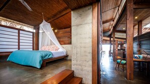 A room with a bed, a bench, a reading area with a chair, and a bookshelf.