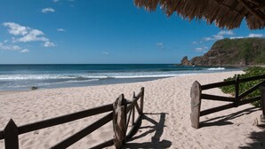 A beach with a wooden fence and a thatched roof structure.