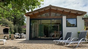 A modern outdoor patio with a wooden pergola, a glass door leading to a covered area, and white lounge chairs.