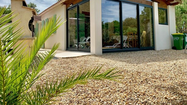 A modern house with a pergola, large glass windows, and a gravel driveway.