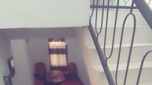 A staircase with a metal railing leading to a room with a red carpet, a table, and two chairs.