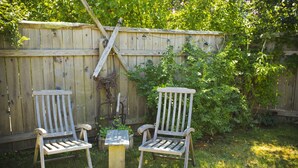 Two wooden chairs and a small table in a backyard with a wooden fence and greenery. - Martha's Vineyard 1BR, Pets Ok, 10 Min walk to beach or Edgartowns shops! (Edgartown)