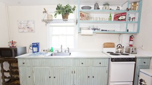 A kitchen with a white stove, sink, and cabinets. There is a window above the sink and a shelf with various kitchen items. - Martha's Vineyard 1BR, Pets Ok, 10 Min walk to beach or Edgartowns shops! (Edgartown)