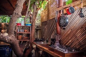 A rustic outdoor kitchen with a gas stove, pots, and a shelf with kitchenware. - La Siesta Troncones  Surf Villa 1 (Troncones)
