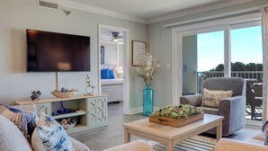 Un salon équipé d’un téléviseur à écran plat, d’une table basse agrémentée d’objets décoratifs, d’un canapé et d’un fauteuil. Une grande fenêtre offre une vue sur l’extérieur.
