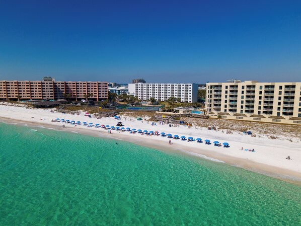 Un complejo turístico en la playa con aguas turquesas cristalinas, playas de arena blanca y varios edificios de hotel al fondo.