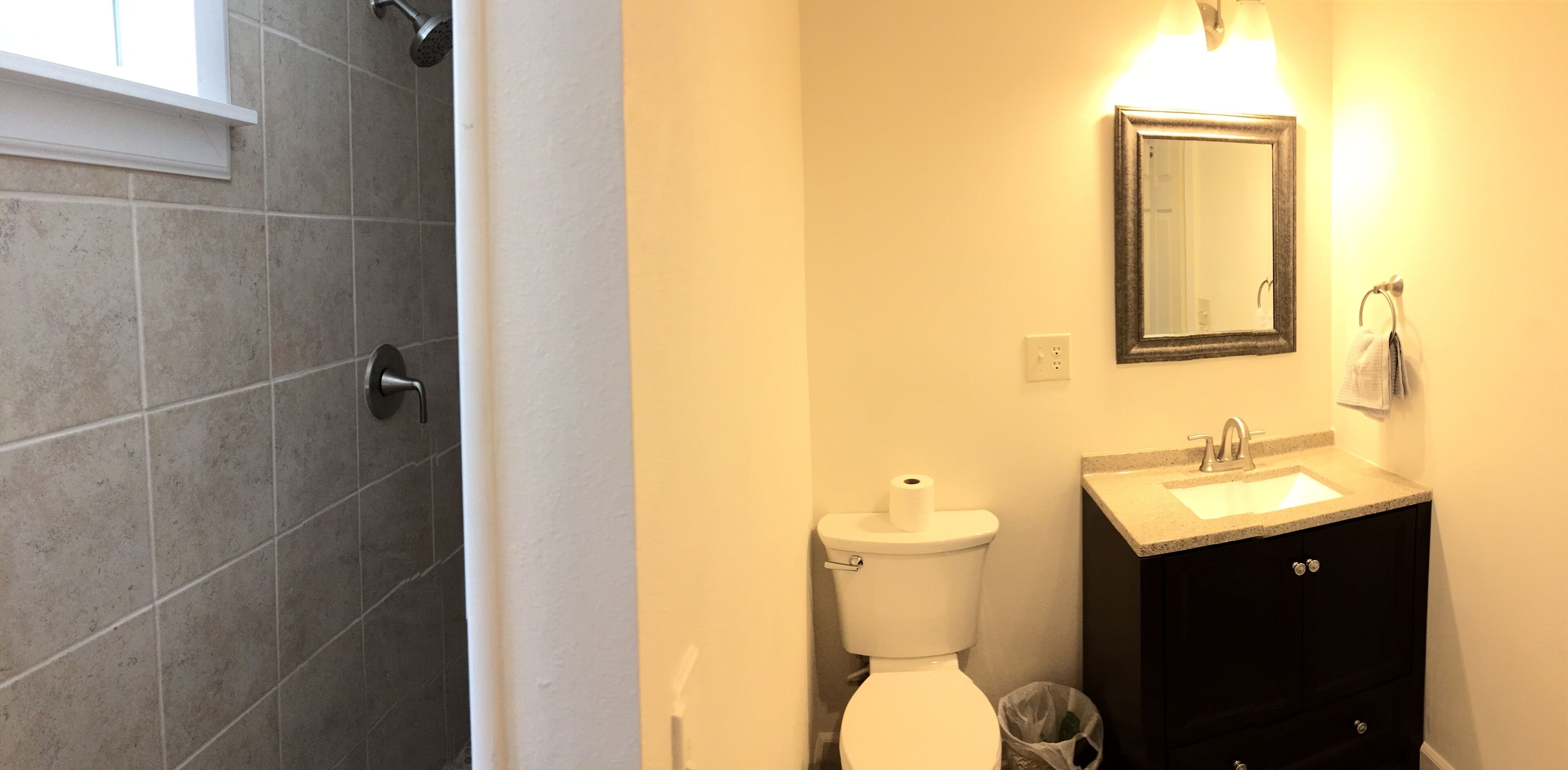 A bathroom with a shower, toilet, sink, and a mirror.