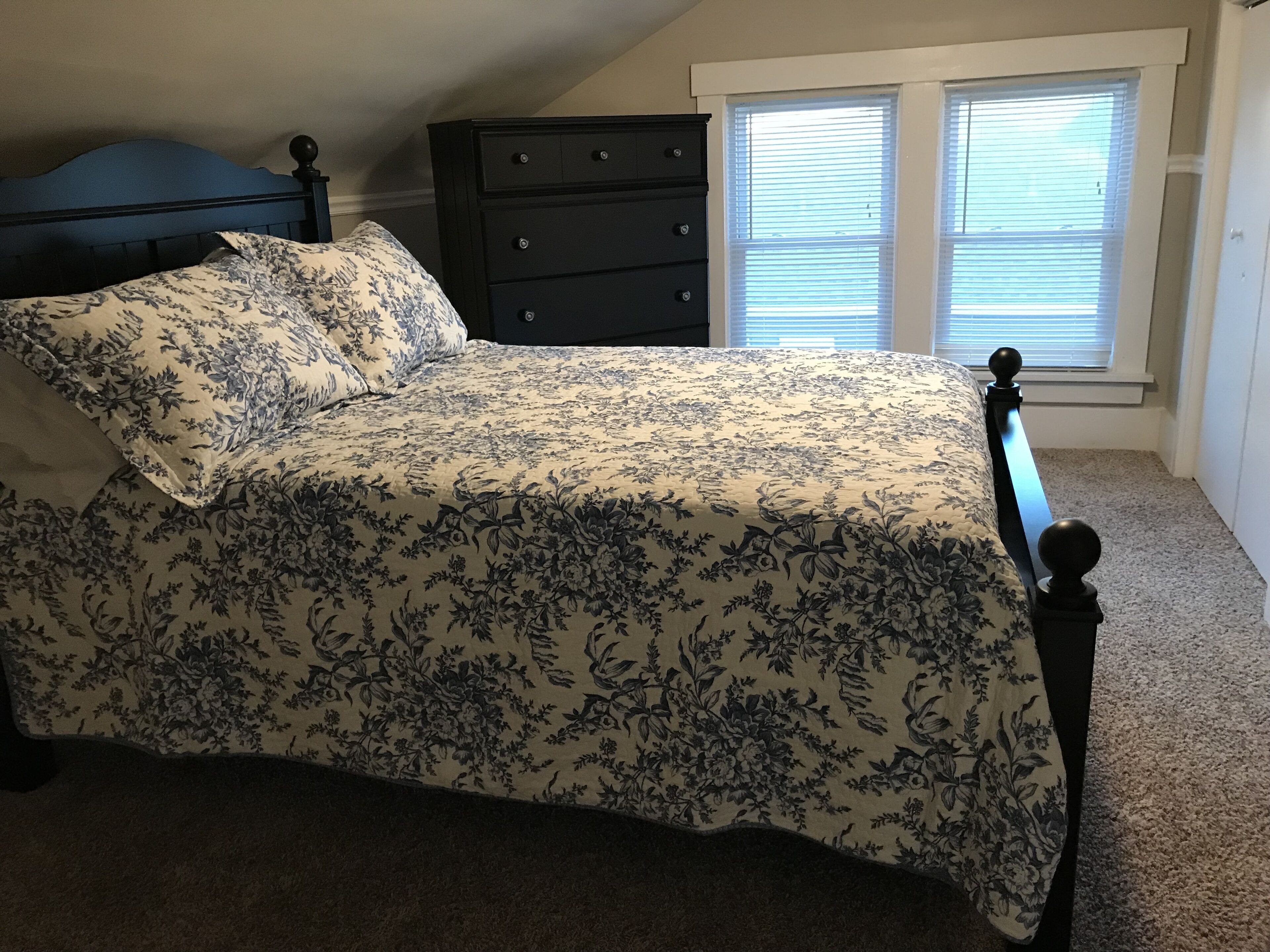 A bedroom with a bed, dresser, and window with blinds.
