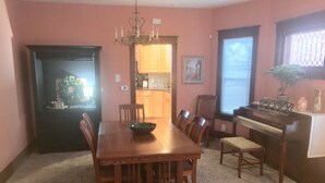 Un comedor con una mesa y sillas de madera, una araña, un piano y una cocina al fondo.