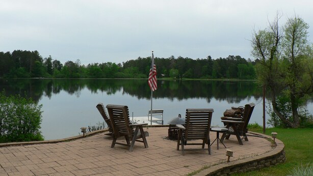 A lakeside patio with outdoor furniture and an American flag.