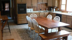 A kitchen with wooden cabinets, a dining table with chairs, a microwave, an oven, and a dishwasher.