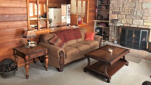 A cozy living room with a wooden wall, a stone fireplace, a sofa, a coffee table, and a side table with a lamp.