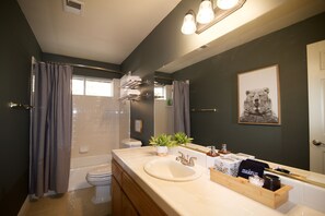 Een moderne badkamer met bad, toilet en wastafel. Boven de wastafel hangt een spiegel en op het aanrecht staat een plant.