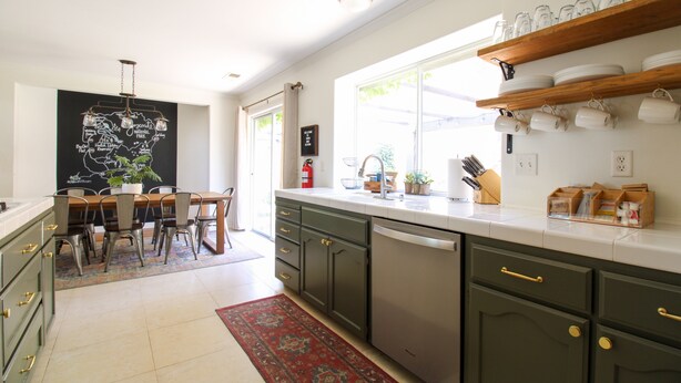 Une cuisine moderne avec un coin repas, dotée d’une grande fenêtre, de meubles en bois et d’un tapis.