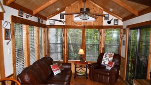 A cozy living room with a brown leather sofa, two leather armchairs, a wooden ceiling fan, and a window with blinds.