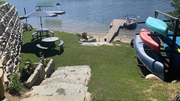 Une terrasse au bord du lac, avec un quai, un espace salon et des kayaks.