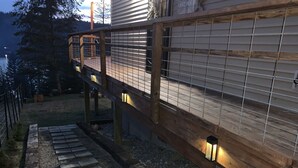Une terrasse en bois avec une rambarde en métal, des marches en pierre et des lampes fixées au mur.