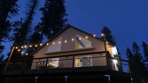 Une cabane dotée d’un balcon, de guirlandes lumineuses et offrant une vue sur de grands arbres.