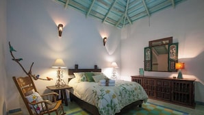 A bedroom with a bed, a rocking chair, a nightstand, a dresser, and wall-mounted lamps.