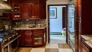 A kitchen with wooden cabinets, a granite countertop, stainless steel appliances, and a view into the adjacent room. - 10 Bedroom Hampton House with a regulation size Pickleball court (Hampton Bays)