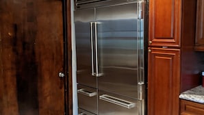 A kitchen with a stainless steel refrigerator, wooden cabinets, and a marble floor. - 10 Bedroom Hampton House with a regulation size Pickleball court (Hampton Bays)