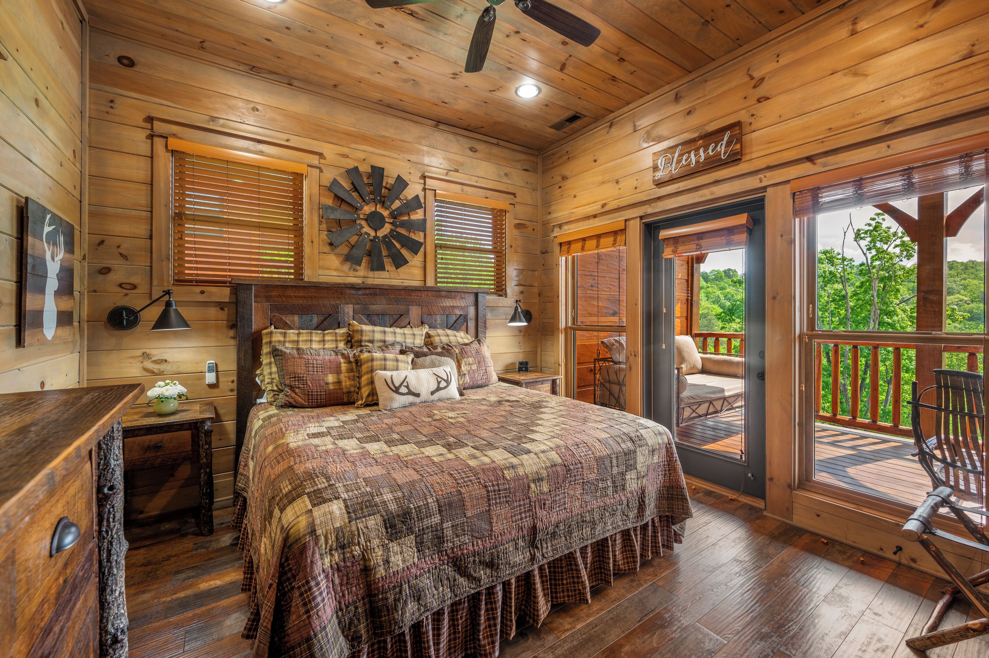 Une chambre confortable, aménagée dans une cabane en bois, avec un grand lit, un ventilateur de plafond et une vue sur l’extérieur.