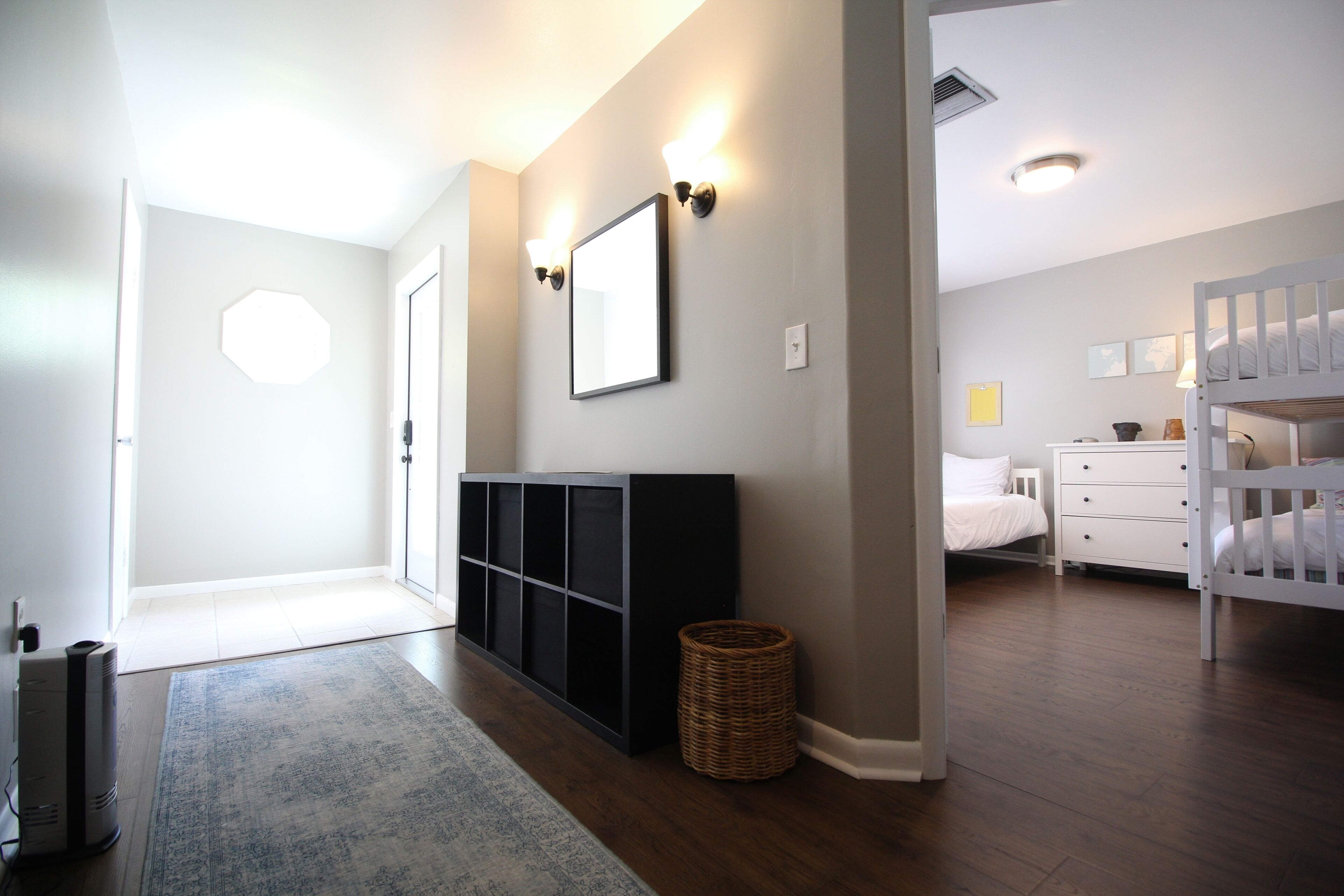 Une chambre d’hôtel moderne avec un plancher en bois, un lit blanc, une commode blanche et une console noire.