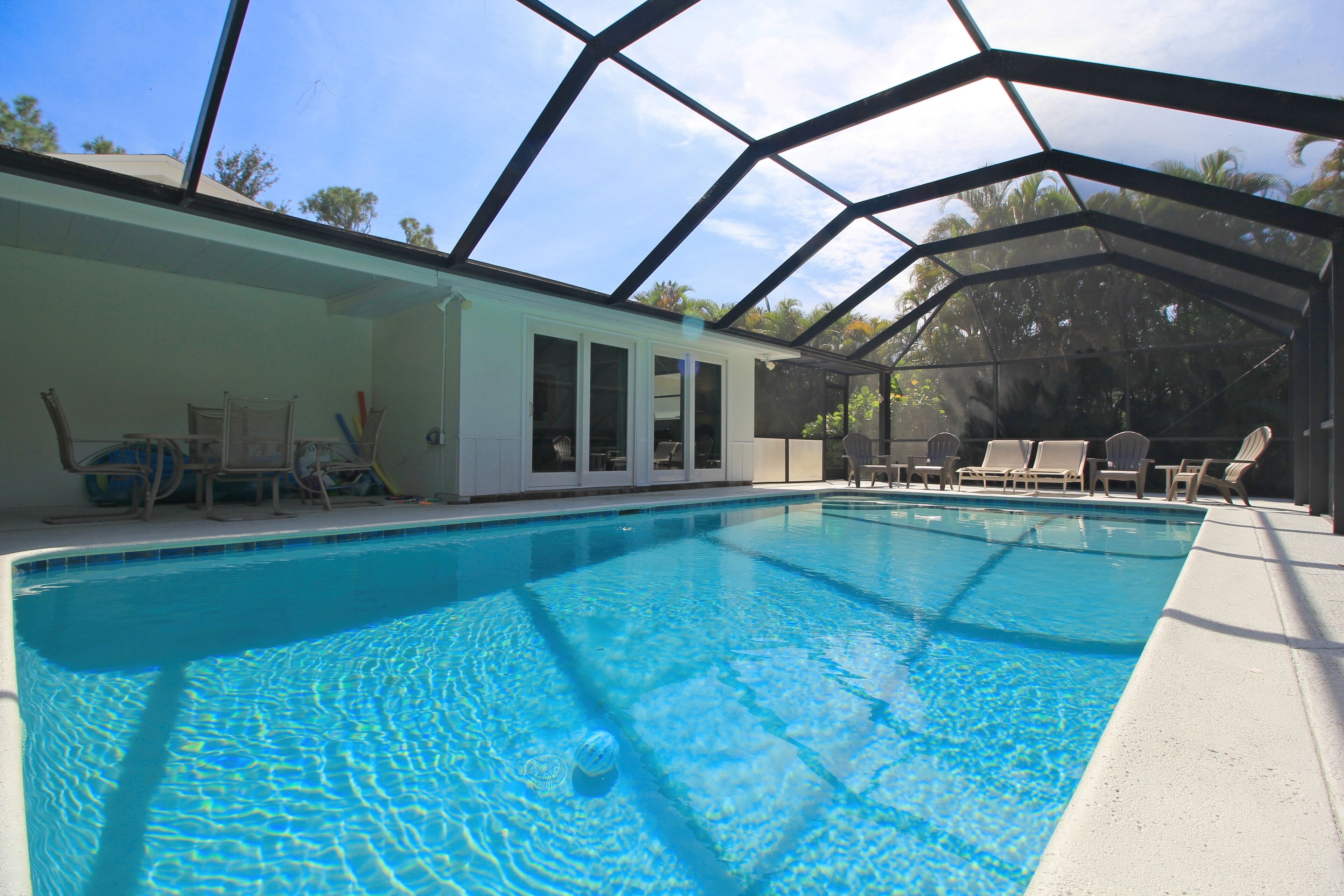 A swimming pool with a glass enclosure, lounge chairs, and a building with large windows.