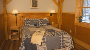 Een slaapkamer met een houten hoofdbord, twee bedlampen, een nachtkastje met boeken en een raam met uitzicht op bomen.